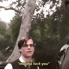a man in a suit and tie is standing in front of a tree and talking to another man .
