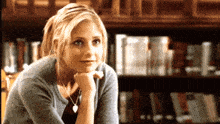 a woman with her hand on her chin is sitting in front of a bookshelf