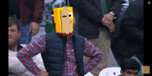 a man in a plaid shirt with a yellow box on his head