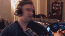 a man wearing headphones and a hat stands in front of a microphone in a living room
