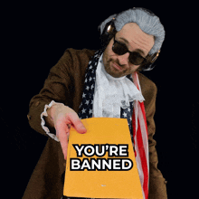a man in a wig and sunglasses is holding a yellow envelope that says " you 're banned "