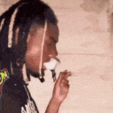 a man with dreadlocks is smoking a cigarette while wearing a black shirt with a logo on it .