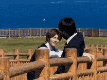 two men are hugging each other behind a wooden fence in front of the ocean .