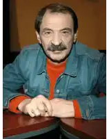 a man with a mustache is sitting at a table with his hands folded