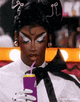 a drag queen is drinking from a purple can with a straw .