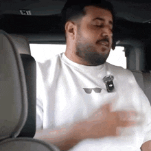 a man with a beard wearing a white shirt with sunglasses on it is sitting in the back seat of a car .