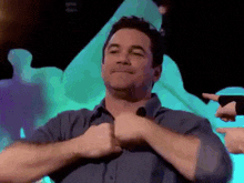 a man in a blue shirt is giving a thumbs up with his hands .