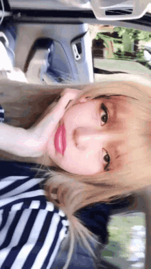 a girl with blonde hair is sitting in a car with her hand on her face .