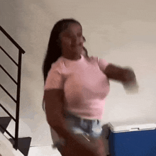 a woman in a pink shirt and shorts is dancing in front of a blue cooler in a room .