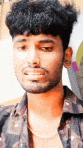 a young man with a beard wearing a plaid shirt looks at the camera
