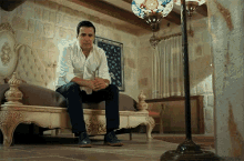 a man in a white shirt sits on a couch in a room