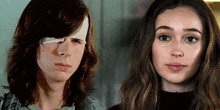 a man with a bandage on his eye and a woman with long hair are looking at the camera .