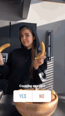a woman in a black hoodie is holding two bananas in front of a bowl and a yes or no question