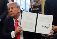 a man in a suit and red tie is holding a signed document .