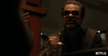 a man with a beard and sunglasses is holding a bottle and a glass with a netflix logo behind him