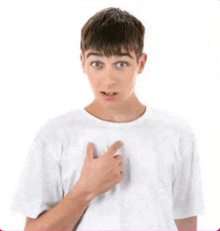 a young boy in a white t-shirt is pointing at his chest .