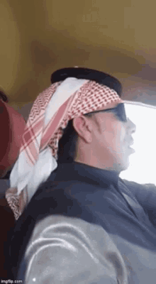 a man wearing a head scarf and sunglasses is sitting in a car .