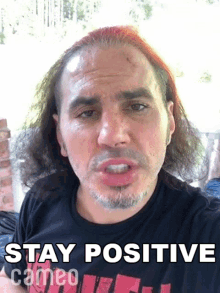 a man with red hair is wearing a black shirt that says " stay positive "