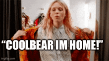 a woman is trying on a jacket in a dressing room with the words `` coolbear im home '' written above her .
