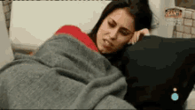 a woman wrapped in a blanket is laying on a couch with her head on a pillow .