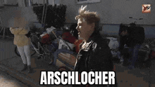 a woman is standing in front of a pile of junk and a sign that says arschlocher on it .