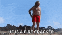 a man in a bikini is standing on a beach with a drone behind him and the words he is a fire cracker .