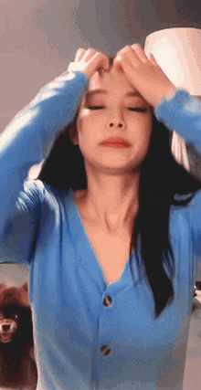 a woman in a blue cardigan is making a heart shape with her hands on her forehead