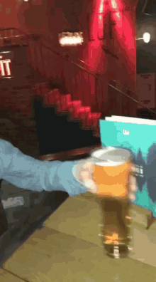 a person holding a glass of beer in front of a sign that says the