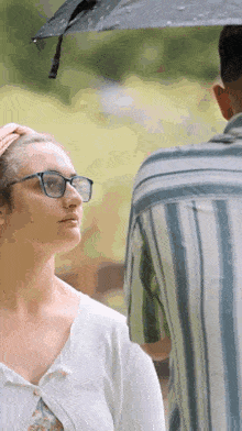 a woman wearing glasses is standing next to a man holding an umbrella over her head .