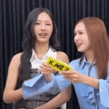 two women are standing next to each other in front of a black curtain and holding a yellow object .