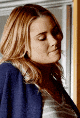 a woman wearing a blue sweater and a striped shirt looks down