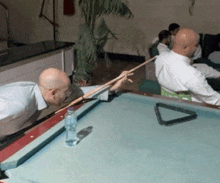two men are playing pool with a bottle of water in the middle