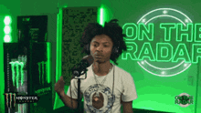 a man wearing headphones stands in front of a microphone in front of a sign that says on the radar