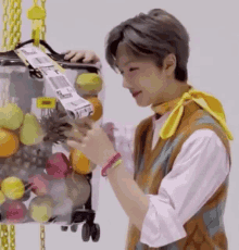 a young man is standing next to a container of fruit and holding a piece of tape .