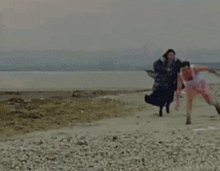 a man and a woman are walking on a beach near the water .