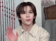 a young man in a white shirt is waving his hand in front of a wooden curtain