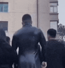 a man in a black suit is walking down a street next to a group of people .