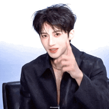 a young man wearing a black jacket and a necklace is giving a thumbs up