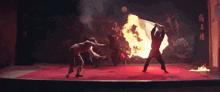 a group of people are performing martial arts on a stage with fire coming out of a flag .