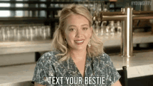 a woman is sitting at a bar and smiling and says text your bestie