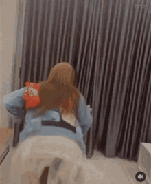 a woman is sitting in front of a curtain with a bag of chips on her back ..