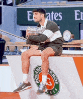 a man is sitting on a podium holding a trophy in front of a sign that says emirates