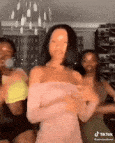 a woman in a pink off the shoulder dress is dancing with three other women .