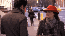 a woman wearing a red hat stands next to a man on a sidewalk