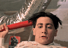 a man is holding a red object in front of his head with a picture of a man on the wall in the background