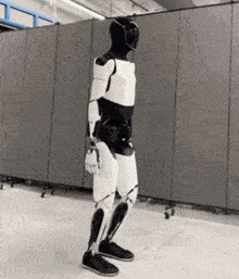 a black and white robot is standing in front of a gray wall