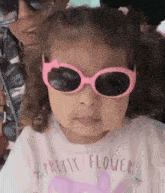 a little girl wearing pink sunglasses and a pretty flower shirt .