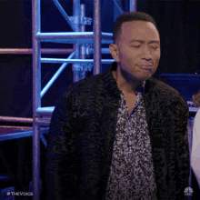 a man with his eyes closed is wearing a black jacket and a floral shirt ..