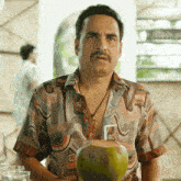a man in a colorful shirt is holding a coconut with a straw in it