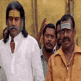 a group of men are standing in a line and one of them has a gold necklace